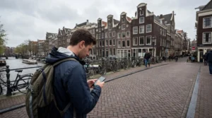 Tourist using smartphone with mobile internet along a canal in Amsterdam Netherlands.