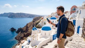 Traveler using mobile data in Greece with the Aegean Sea and white Greek island buildings in the background