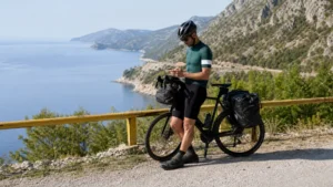 Touring cyclist checking a phone beside a Croatian coastal route.