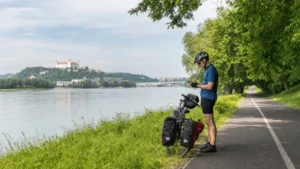 Cyclist safely stopped beside the Danube checking a smartphone mounted near a touring bicycle.