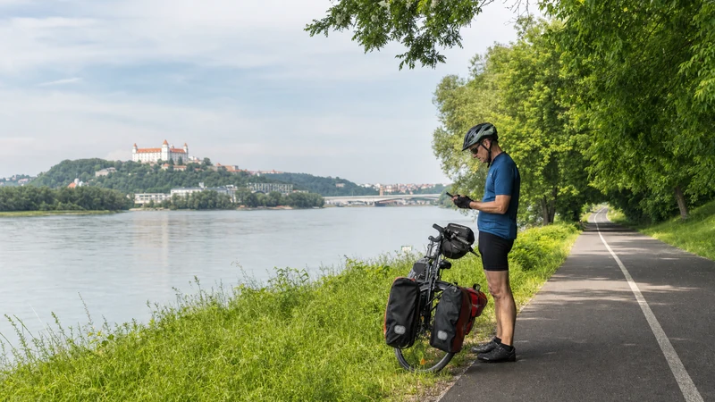 Cyclist safely stopped beside the Danube checking a smartphone mounted near a touring bicycle.
