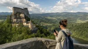 Visitor checking a smartphone at a viewpoint overlooking Orava Castle and its valley.