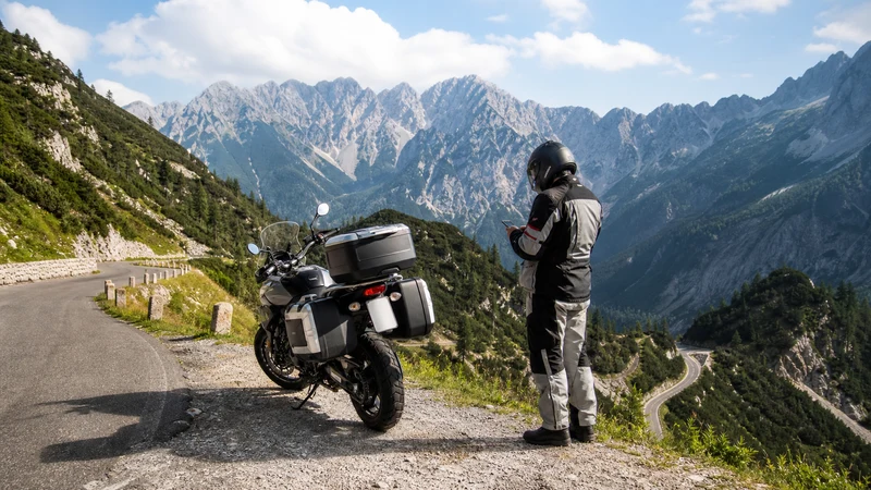 Motorcyclist checking a smartphone at a safe stop on Slovenia’s Vršič Pass.