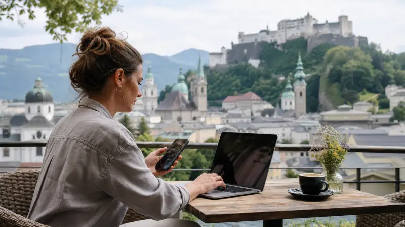Remote-working traveller using a laptop and smartphone overlooking Salzburg, Austria