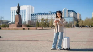 Traveller with a suitcase using a smartphone in an Aktobe public square.