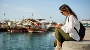 Traveller using a smartphone in traveller near Al Khor harbour and fishing boats