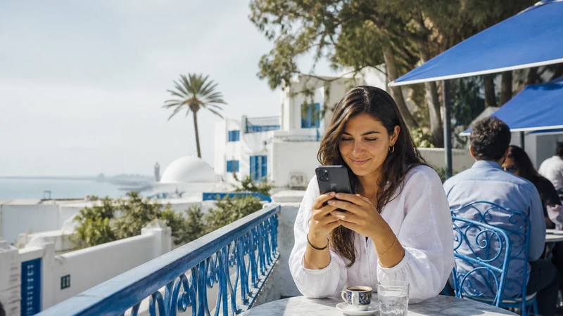 Traveller using a smartphone at a Tunisian café overlooking white-and-blue architecture.