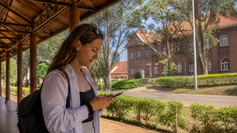 Traveller using a smartphone on a leafy walkway in Huye