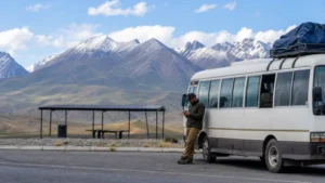 Overland traveller using a smartphone beside a minibus on the Kyrgyzstan route.