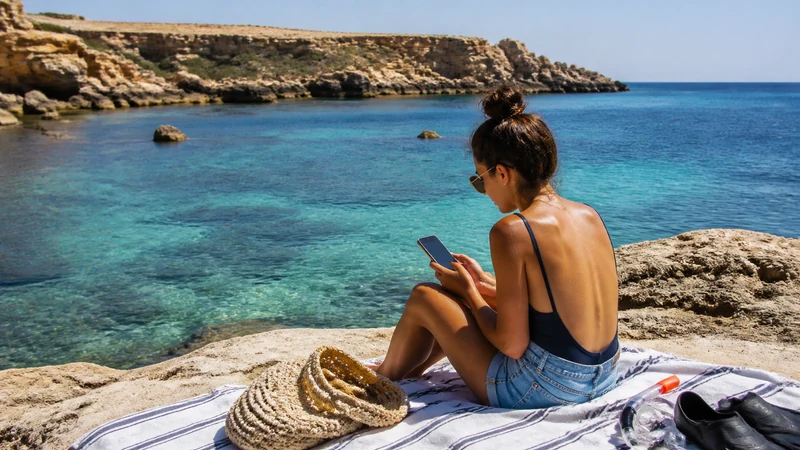 Traveller using a smartphone beside a rocky bay in Malta