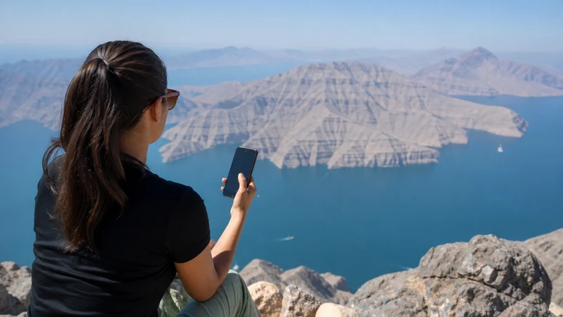 Traveller using a smartphone during visitor overlooking Musandam fjords
