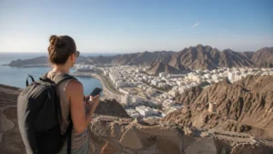 Traveller using a smartphone during coverage planning above Omani coast and mountains