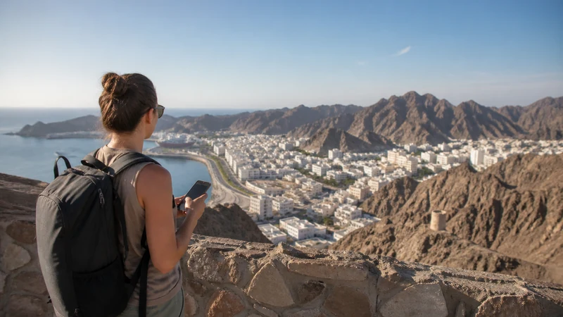 Traveller using a smartphone during coverage planning above Omani coast and mountains