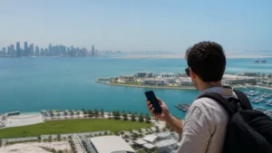 Traveller using a smartphone in traveller overlooking Doha skyline, desert and coast from an elevated viewpoint