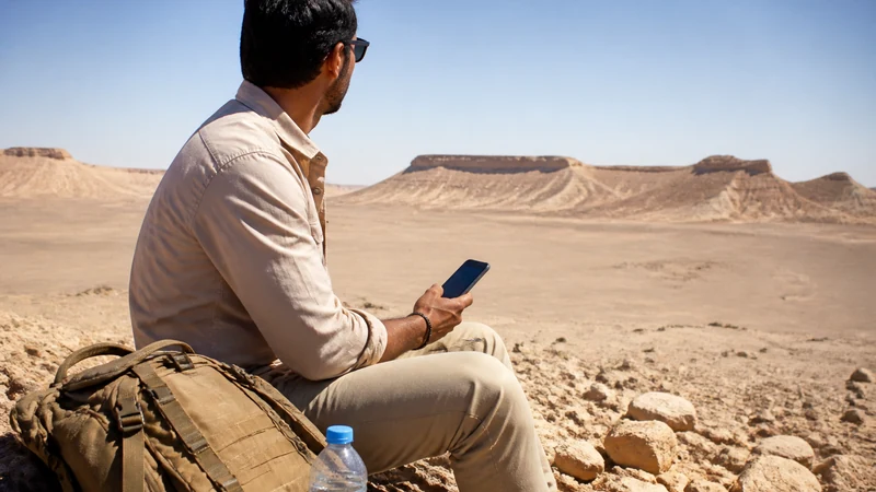 Traveller using a smartphone in a sparsely populated Qatar desert landscape