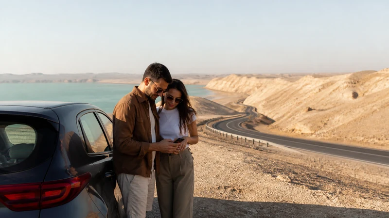 Traveller using a smartphone in travellers checking navigation beside a parked rental car on a Qatar road