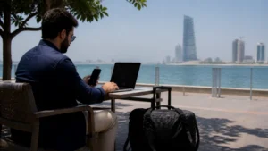 Remote worker using a phone and laptop beside the Jeddah waterfront.