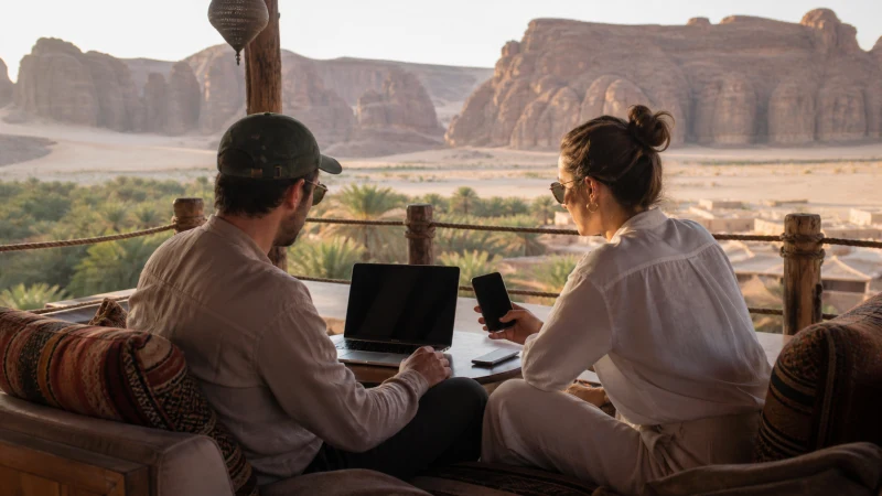 Travellers sharing mobile data with a laptop overlooking AlUla.
