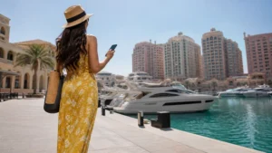 Traveller using a smartphone in visitor beside yachts and pastel buildings at the Pearl-Qatar